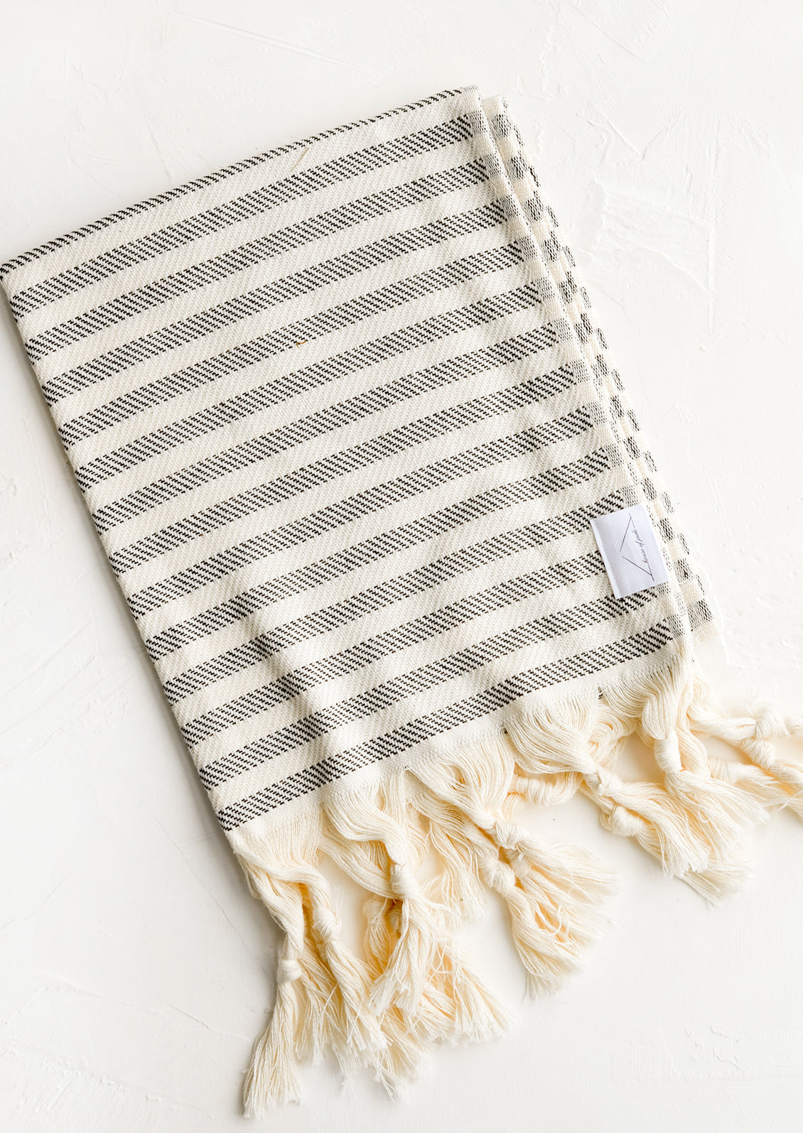 A turkish hand towel in natural with black stripes with natural fringed trim.