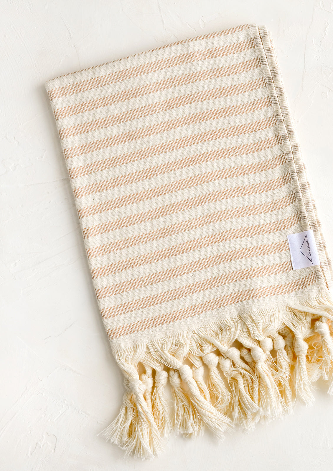 A turkish hand towel in natural with tan stripes with natural fringed trim.