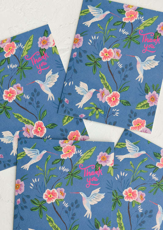 A set of blue greeting cards with hummingbird floral print, pink script at corner reads "Thank you".