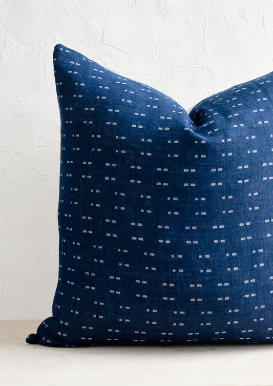 A square throw pillow with indigo background and white woven dash pattern.