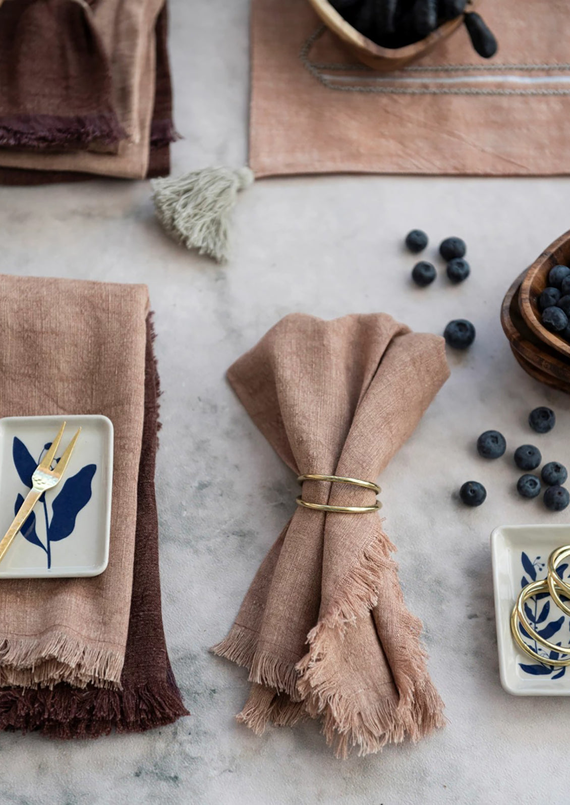 A styled table scene with textiles, ceramics and gold napkin rings.