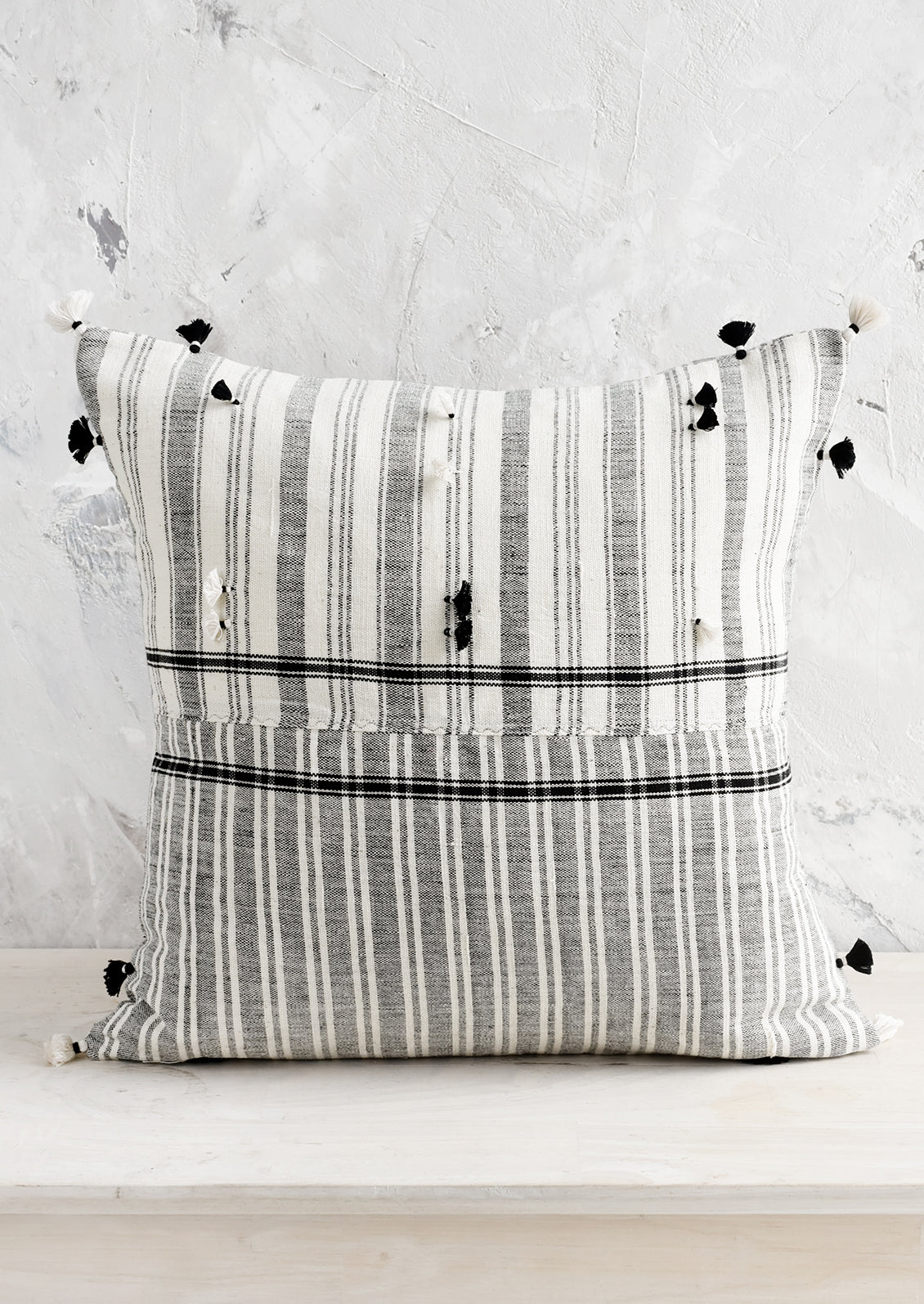 A square throw pillow in black and white madras fabric with tassel detailing throughout.