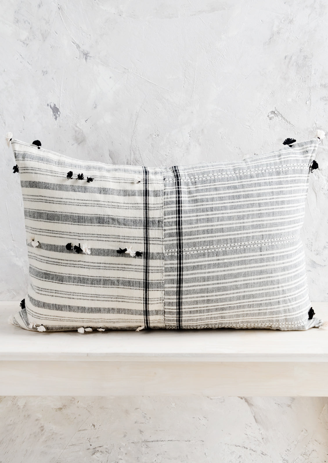 A lumbar throw pillow in black and white madras fabric with tassel detailing throughout.