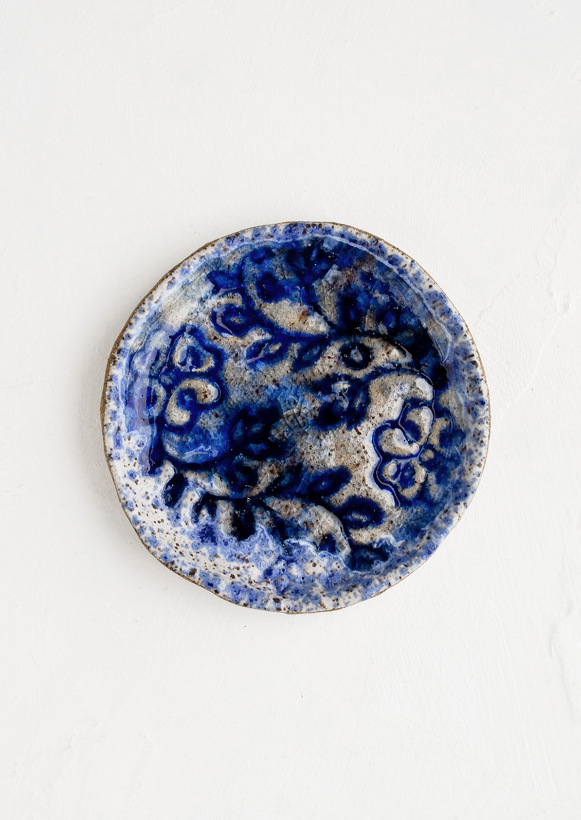 A round ceramic dish with floral imprint and blue glaze.