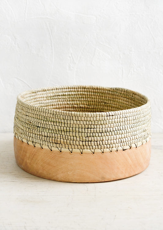 A wide, shallow bowl made from half wood and half woven grass with black thread.