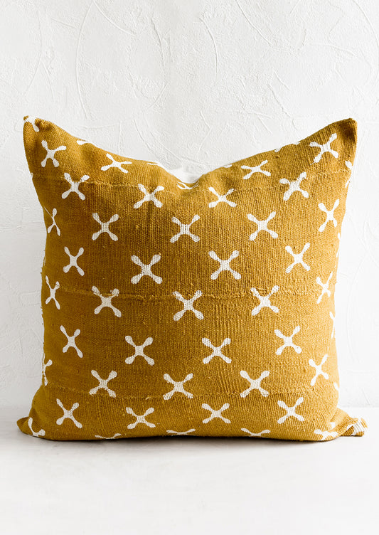 A mustard mudcloth throw pillow with white X pattern.