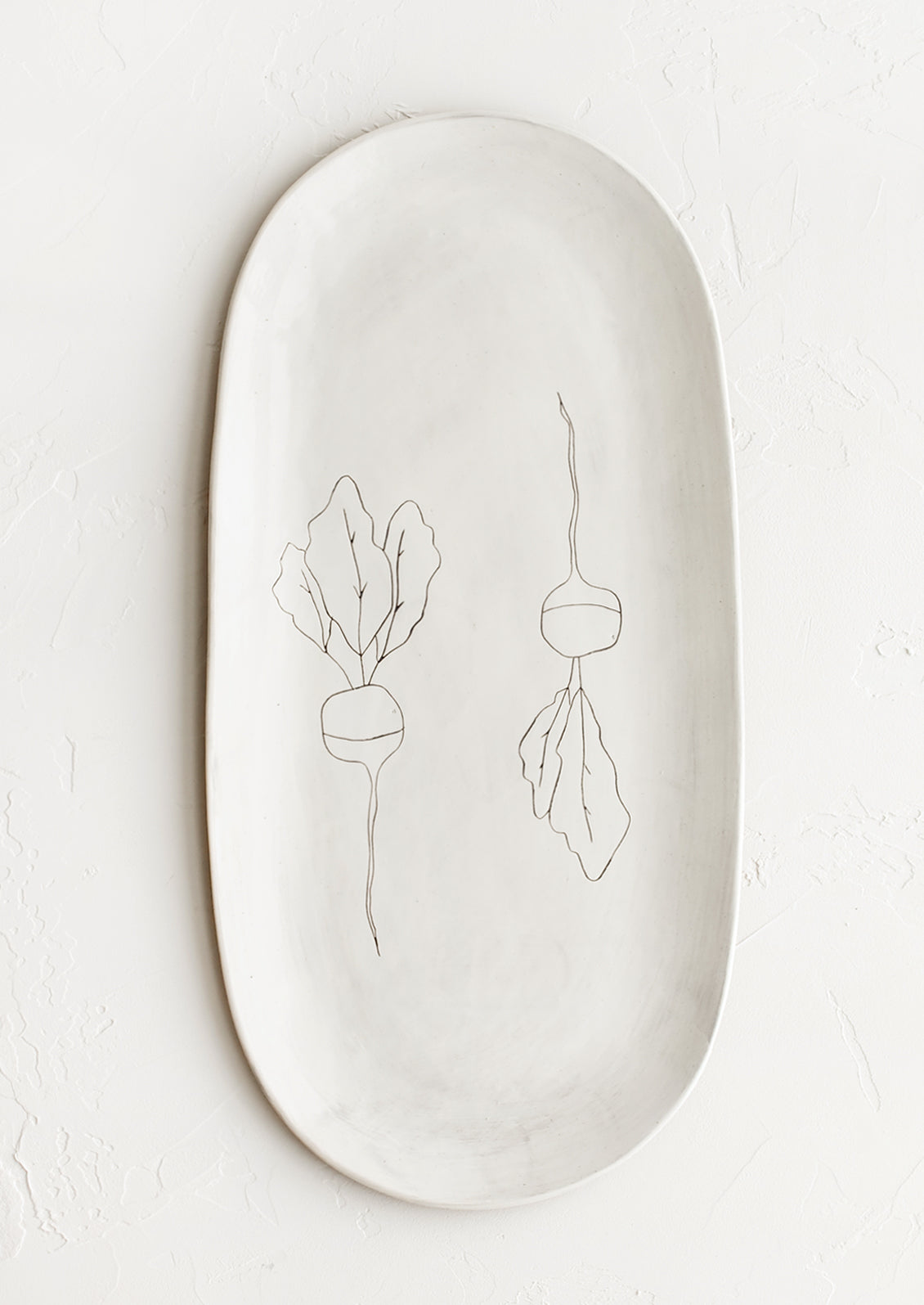 An oval shaped ceramic serving platter with hand drawn radish illustration at center.