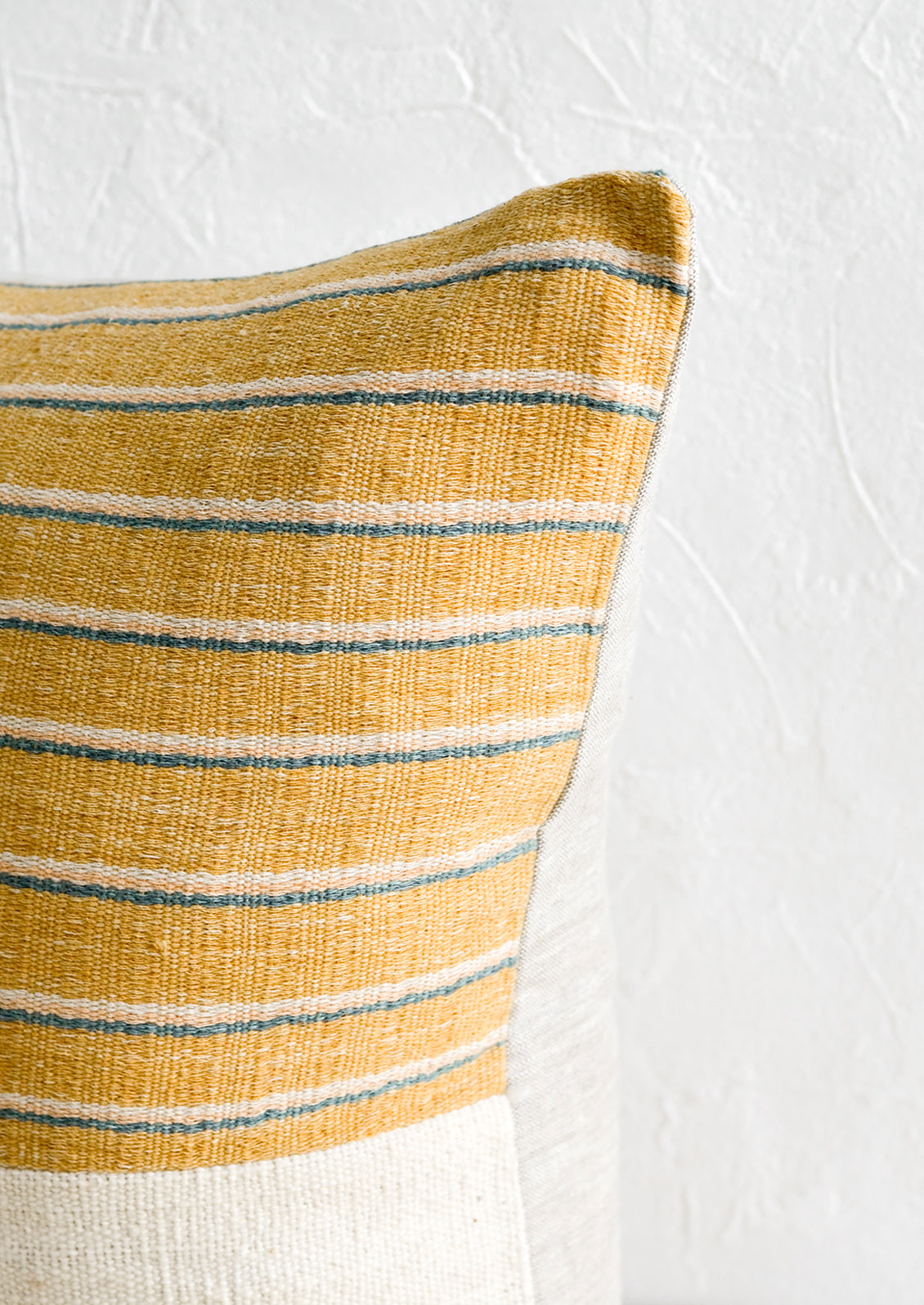 A throw pillow with top half in mustard, ivory & teal striped fabric with natural linen back.