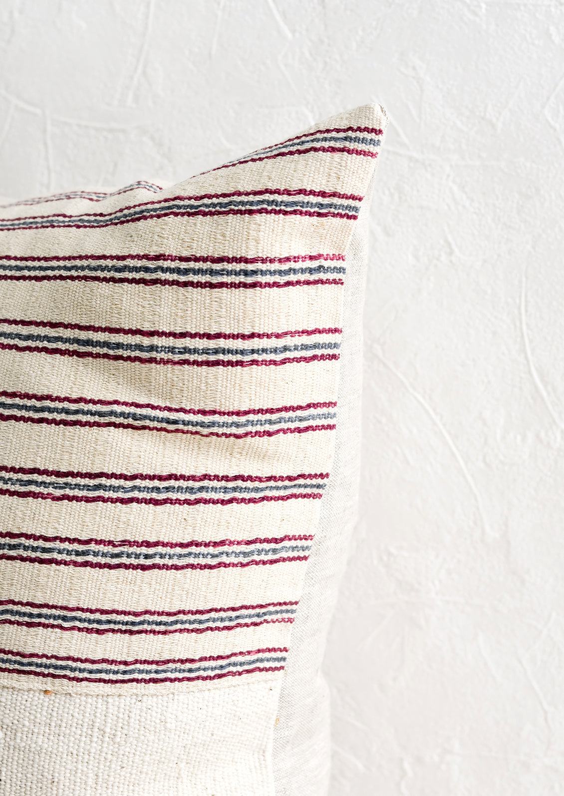 A throw pillow with top half in ivory, red and blue striped fabric and natural linen back.