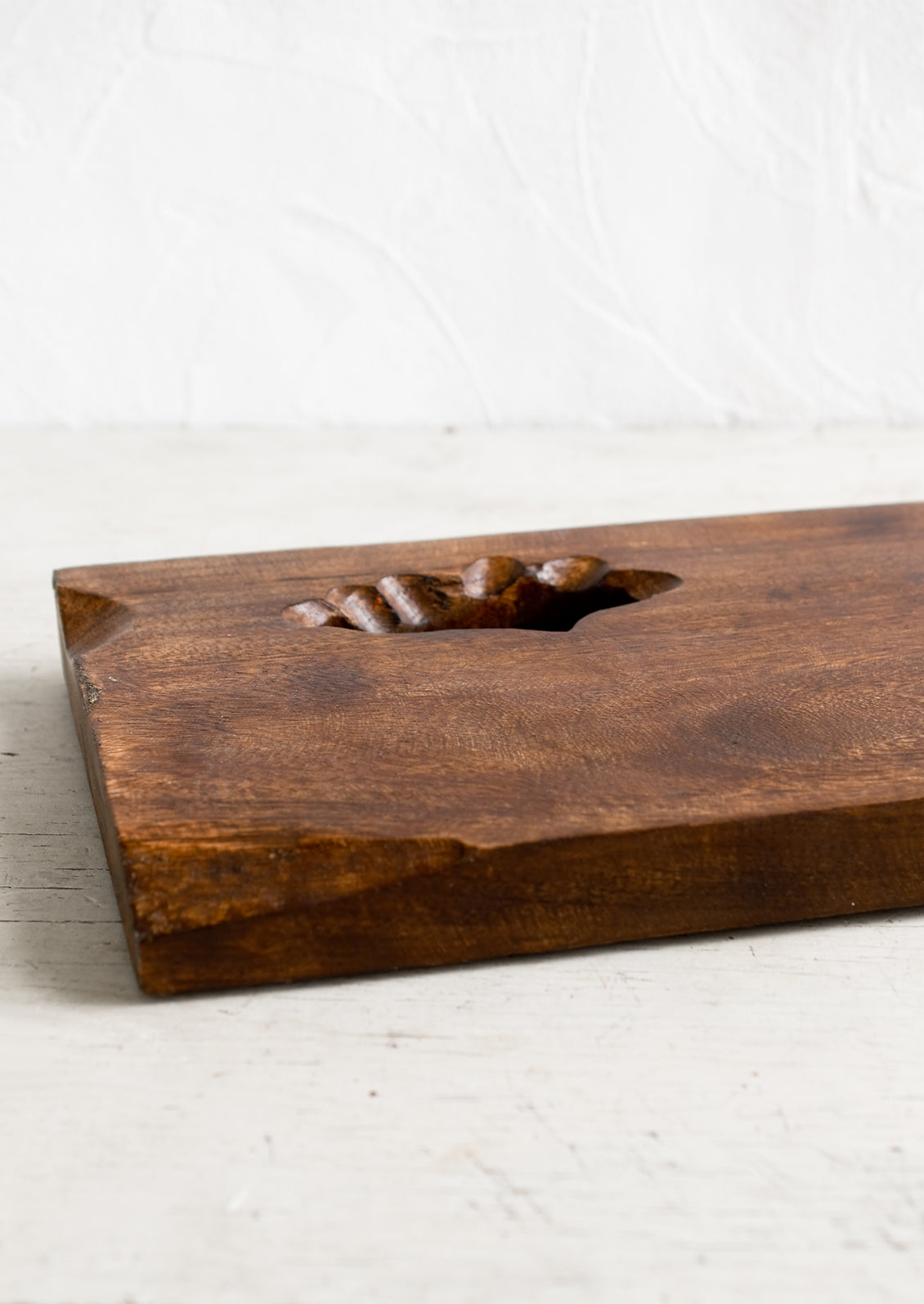 A rectangular wooden cutting board with knot cutout detail.