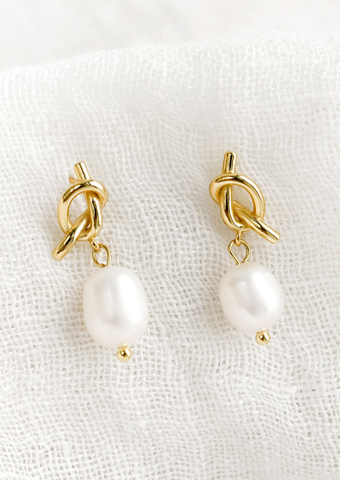 A pair of pearl earrings with knot shaped post in gold.