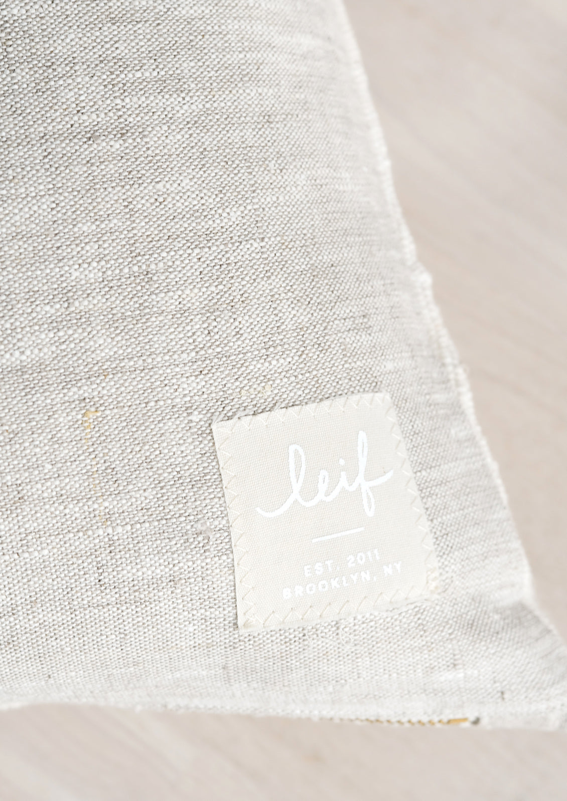 Natural linen with hand-stitched square logo patch at bottom corner.