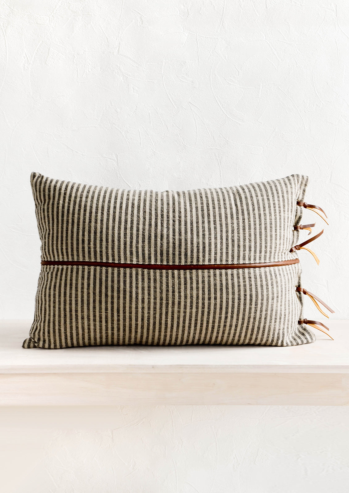 Striped cotton pillow in black and tan with brown leather band detail horizontally across center