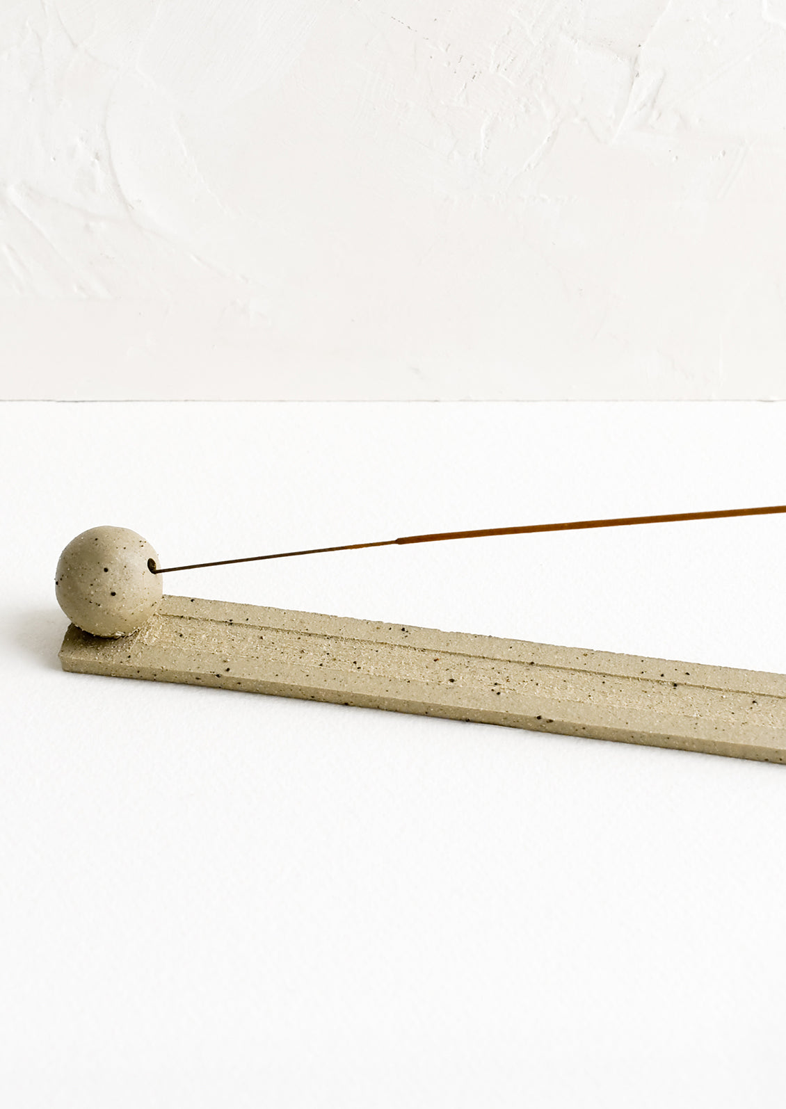 A long, skinny ceramic incense holder with ball detail at one end.