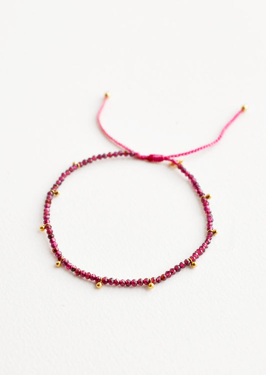 A bracelet of small red gemstones and evenly spaced gold beads.