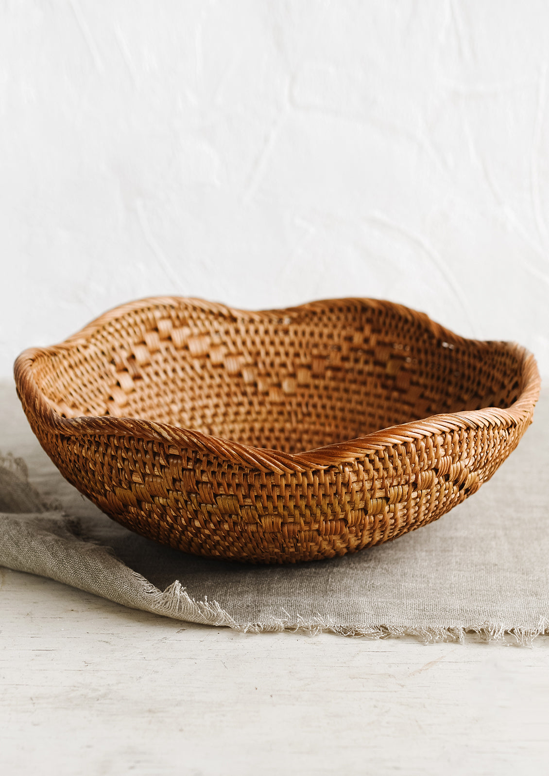 A brown woven shallow rattan basket with wavy edge.