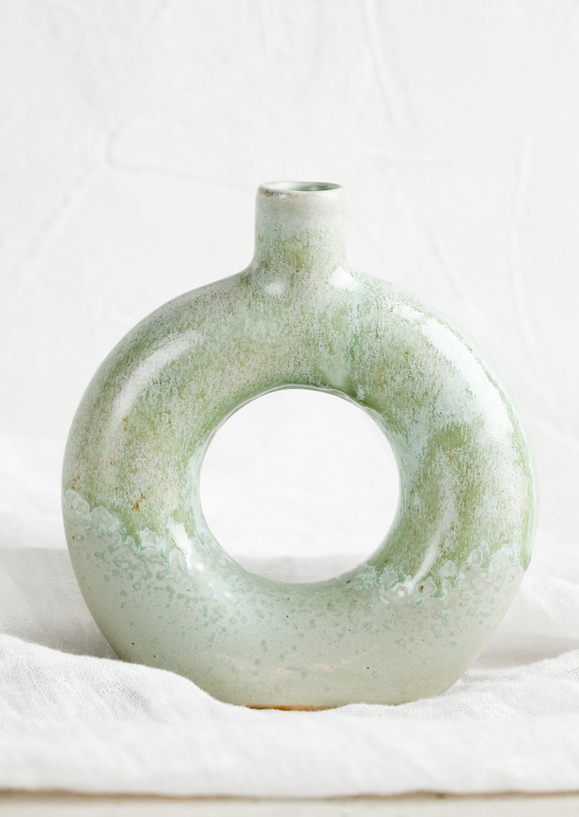 A ceramic vase in mottled aqua glaze with hollow circle shape.