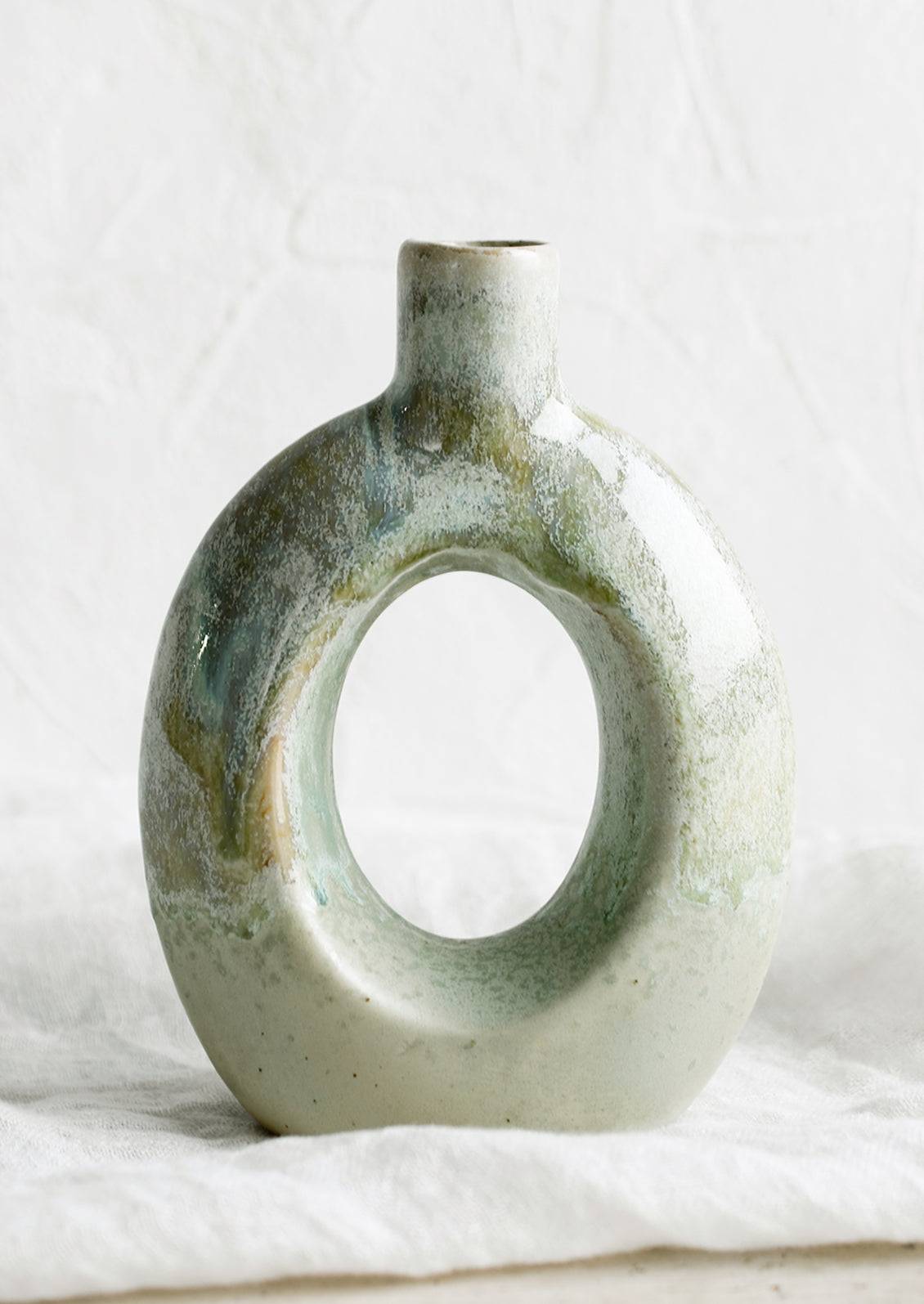 A ceramic vase in mottled aqua glaze with hollow oval shape.