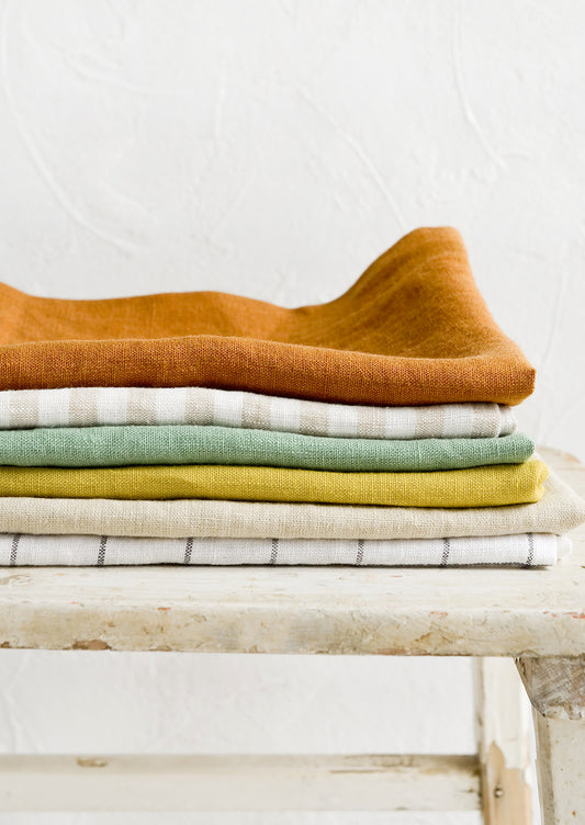 A stack of linen tea towels in a mix of assorted solid colors and patterns.