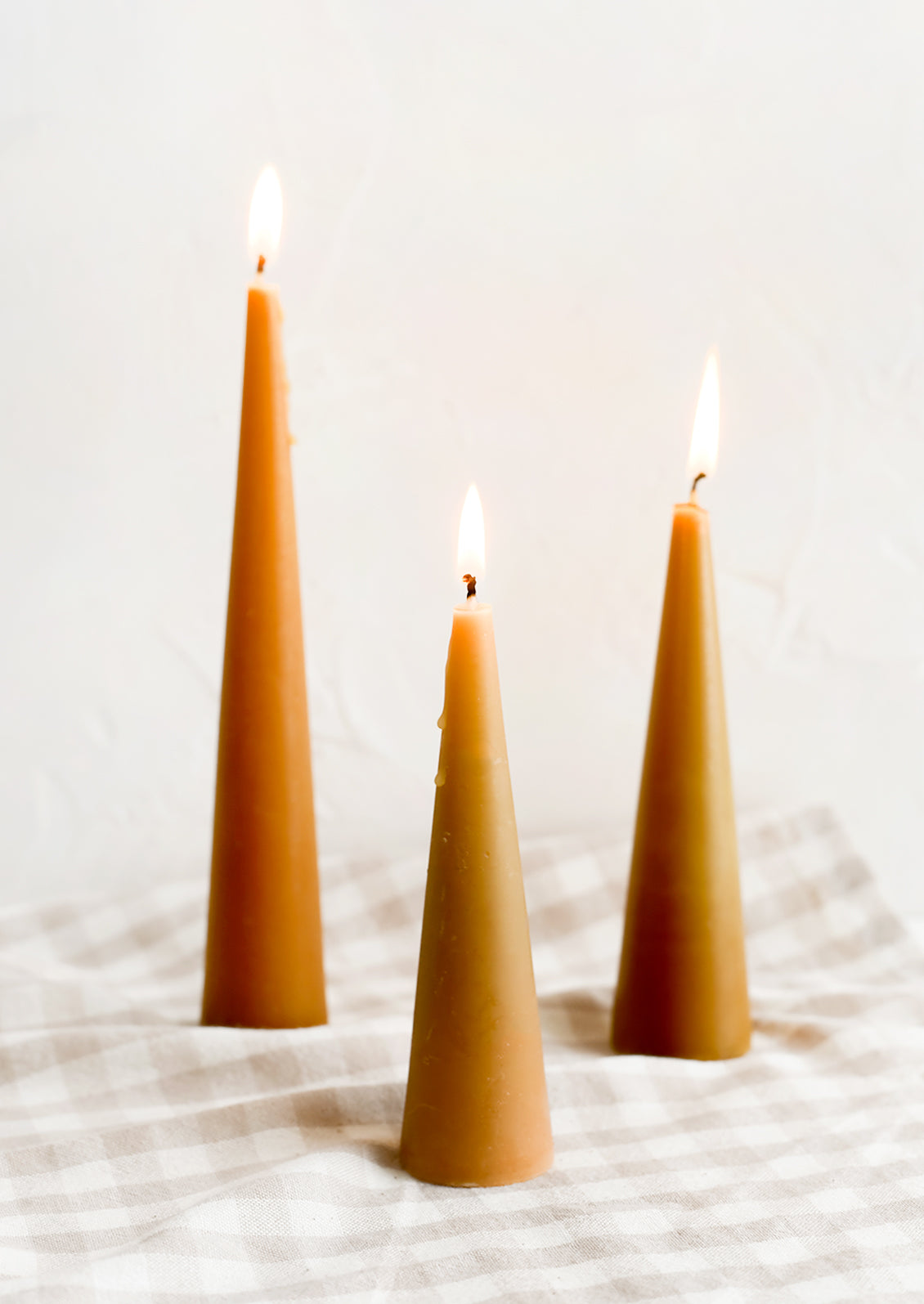 Three lit cone-shaped taper candles in caramel.