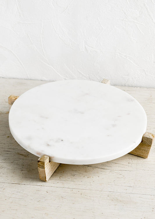 A round white marble riser on wooden X stand.