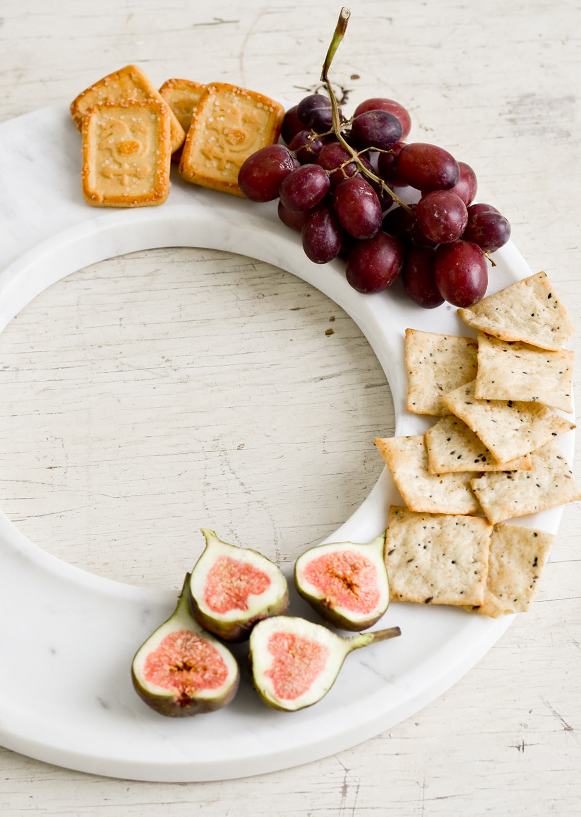 A circular white marble tray covered in crackers, grapes & figs.