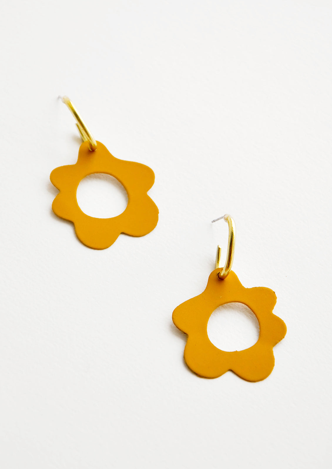 Mustard yellow flower shaped earrings with circular cutouts on small brass open hoops.