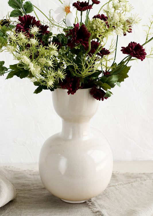 A cream ceramic vase with large bouquet of flowers.