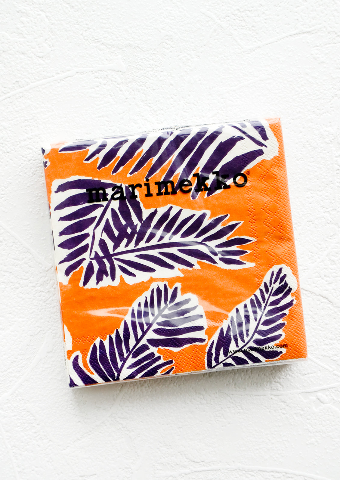 Packaged disposable paper napkins in square cocktail size with orange and purple leaf print.