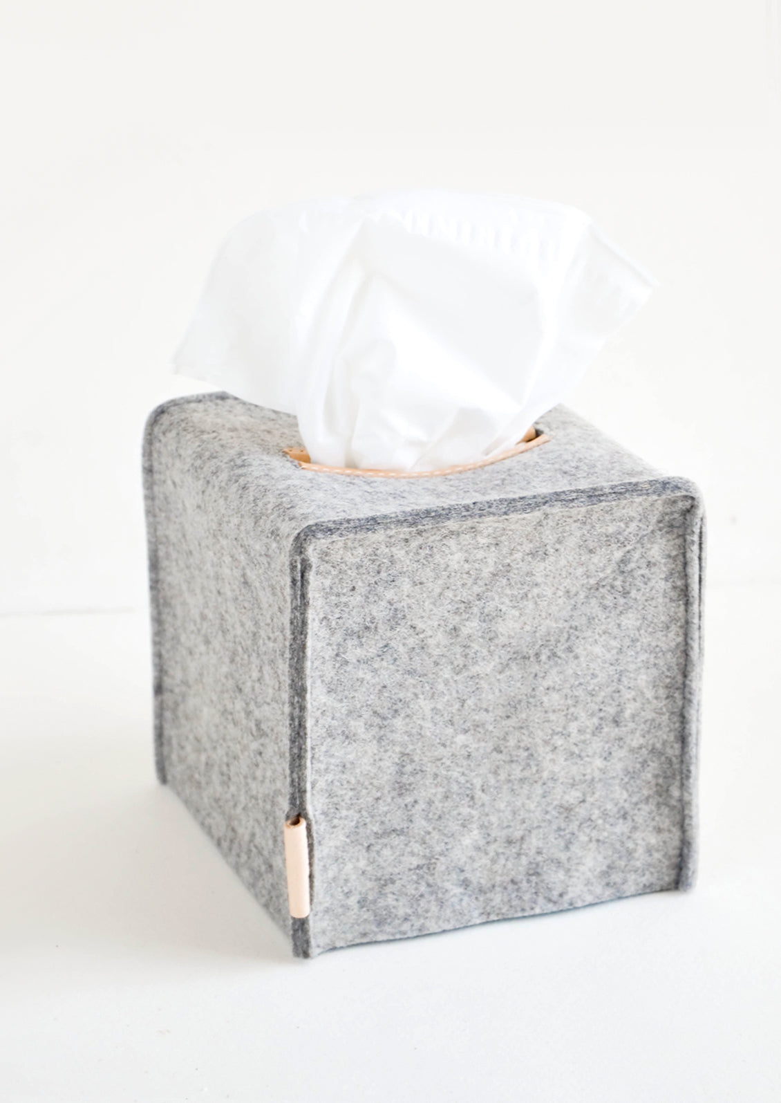 Cube-shaped tissue box cover made from felted wool in heathered dark grey color with leather accents