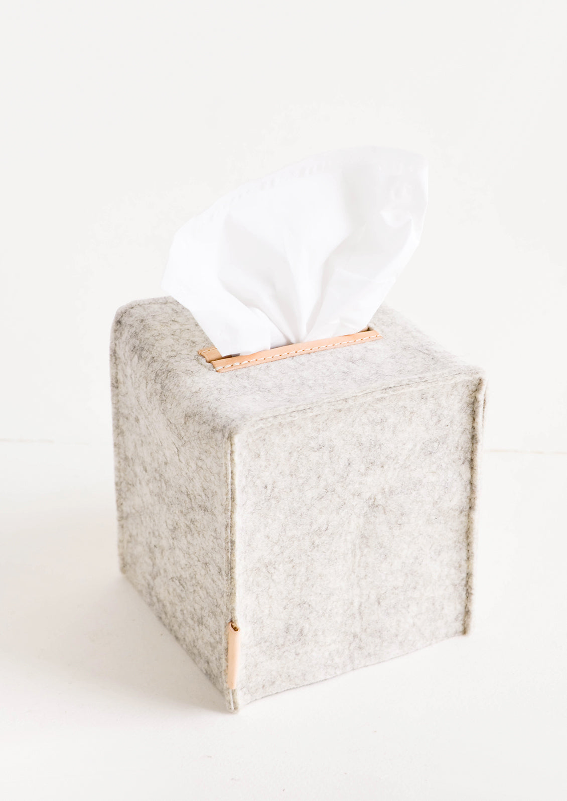 Cube-shaped tissue box cover made from felted wool in heathered light grey color with leather accents