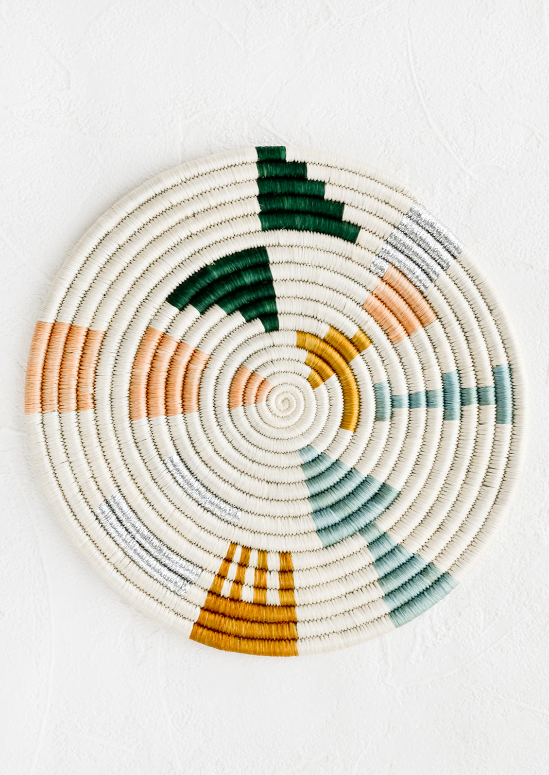 A round trivet in white with metallic and pastel design.