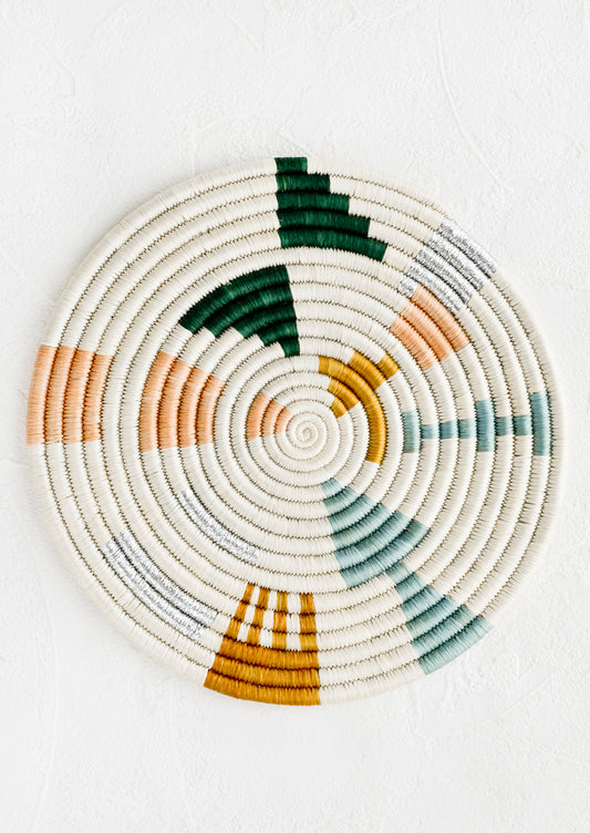 A round trivet in white with metallic and pastel design.