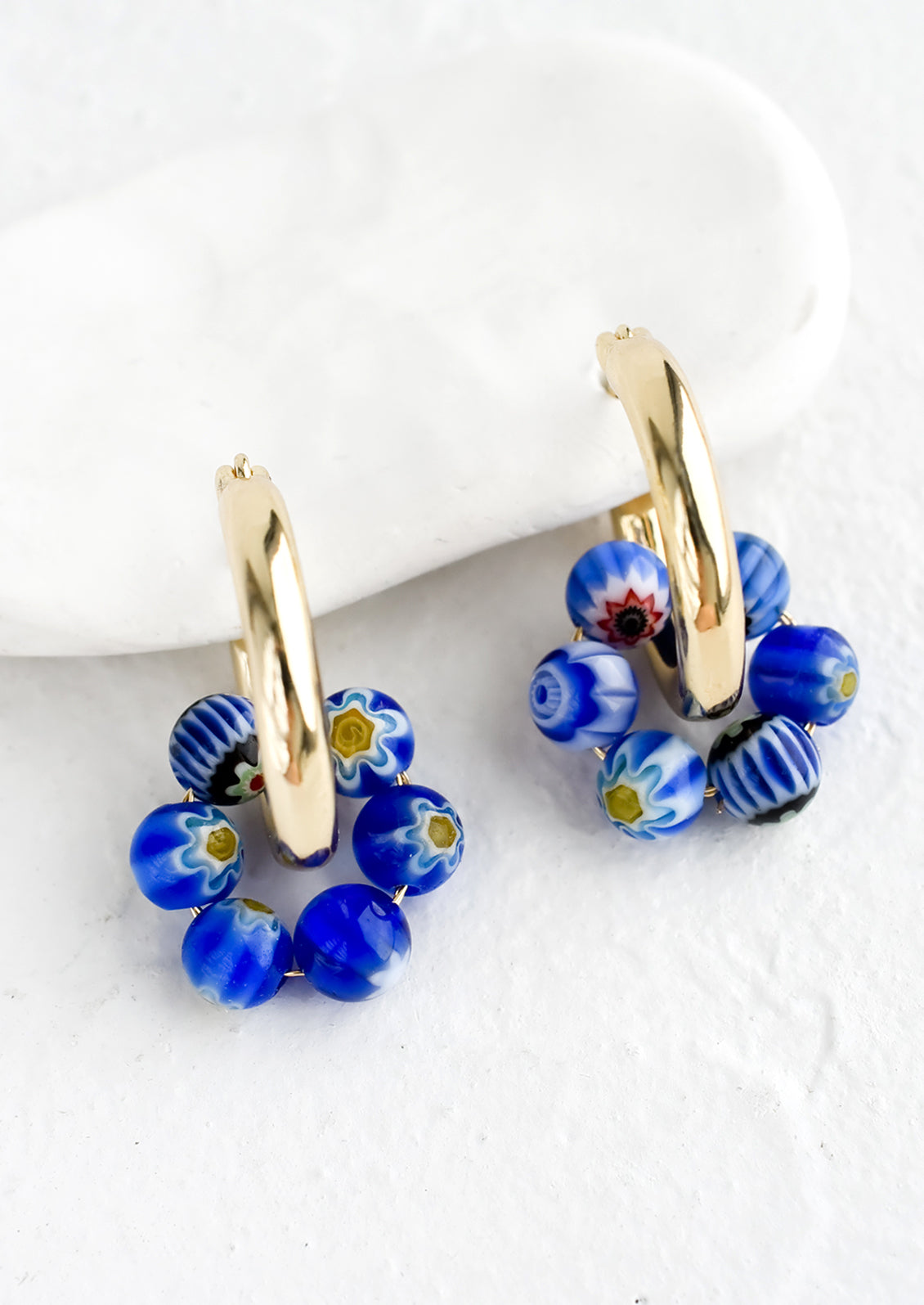 A pair of gold hoop earrings with cobalt millefiore glass beads.