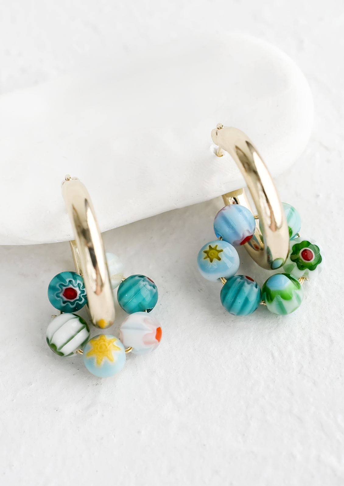 A pair of gold hoop earrings with turquoise millefiore glass beads.