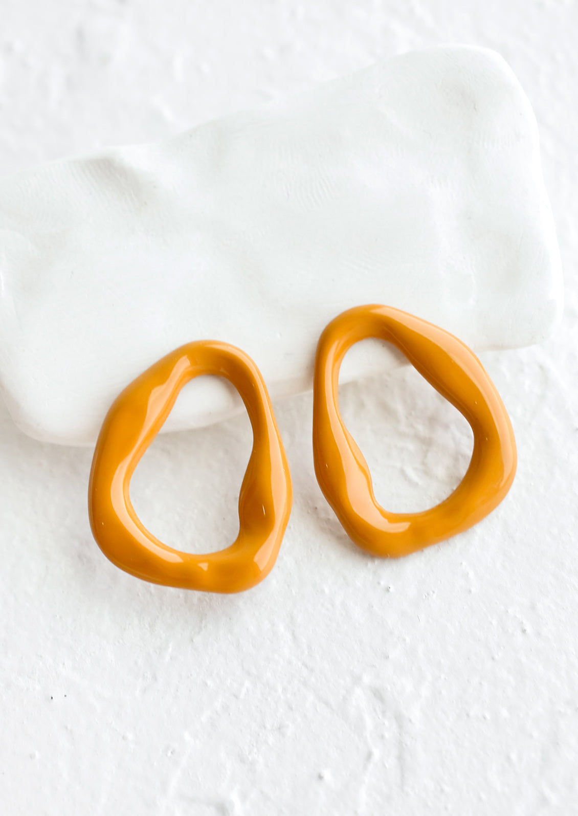 A pair of hollow, circular earrings with rippled texture in mustard hue.