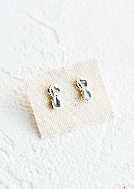 A pair of silver stud earrings on canvas card featuring a drippy, melty appearance.