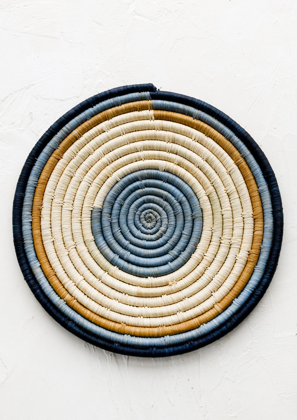 A raffia trivet with concentric blue and tan design.