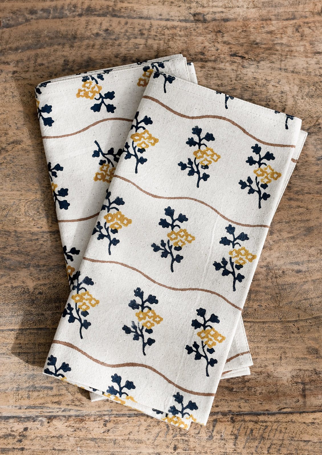 A natural cotton napkin with wavy brown line and navy/mustard flower print.