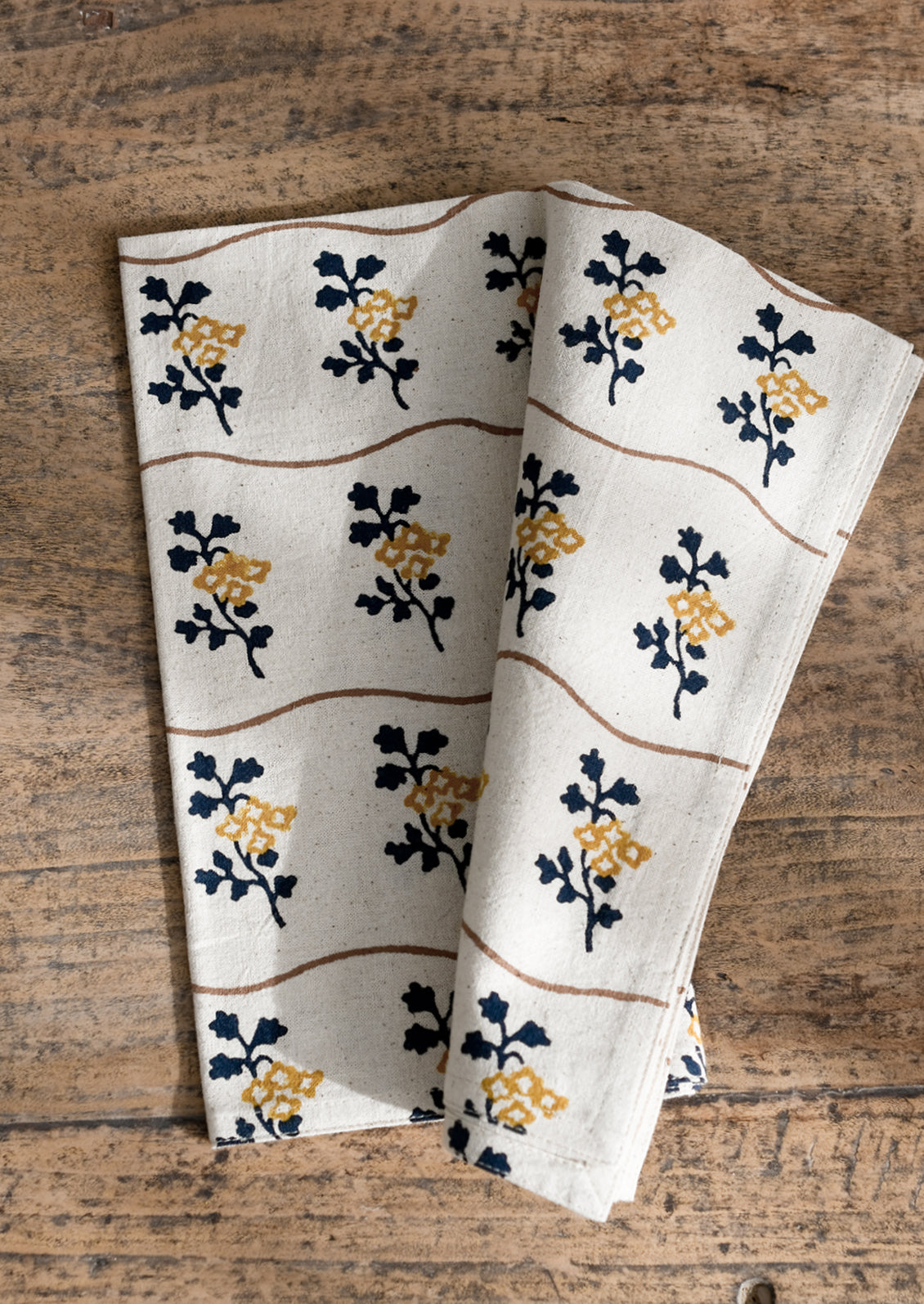 A natural cotton napkin with wavy brown line and navy/mustard flower print.