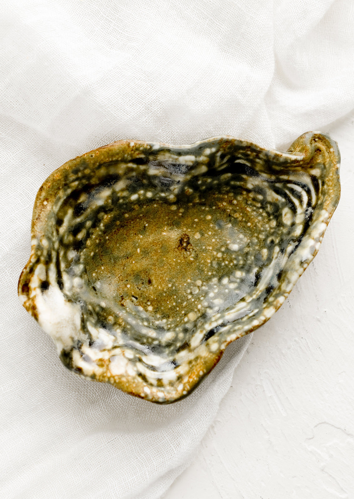 A shallow trinket catchall tray in shape of oyster shell.