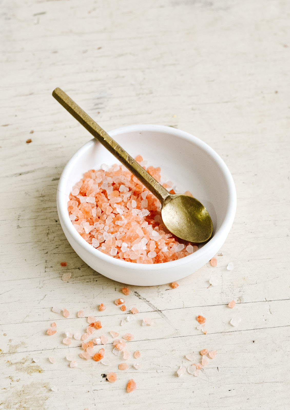 A small white ceramic dish with pink salt and a brass spoon.