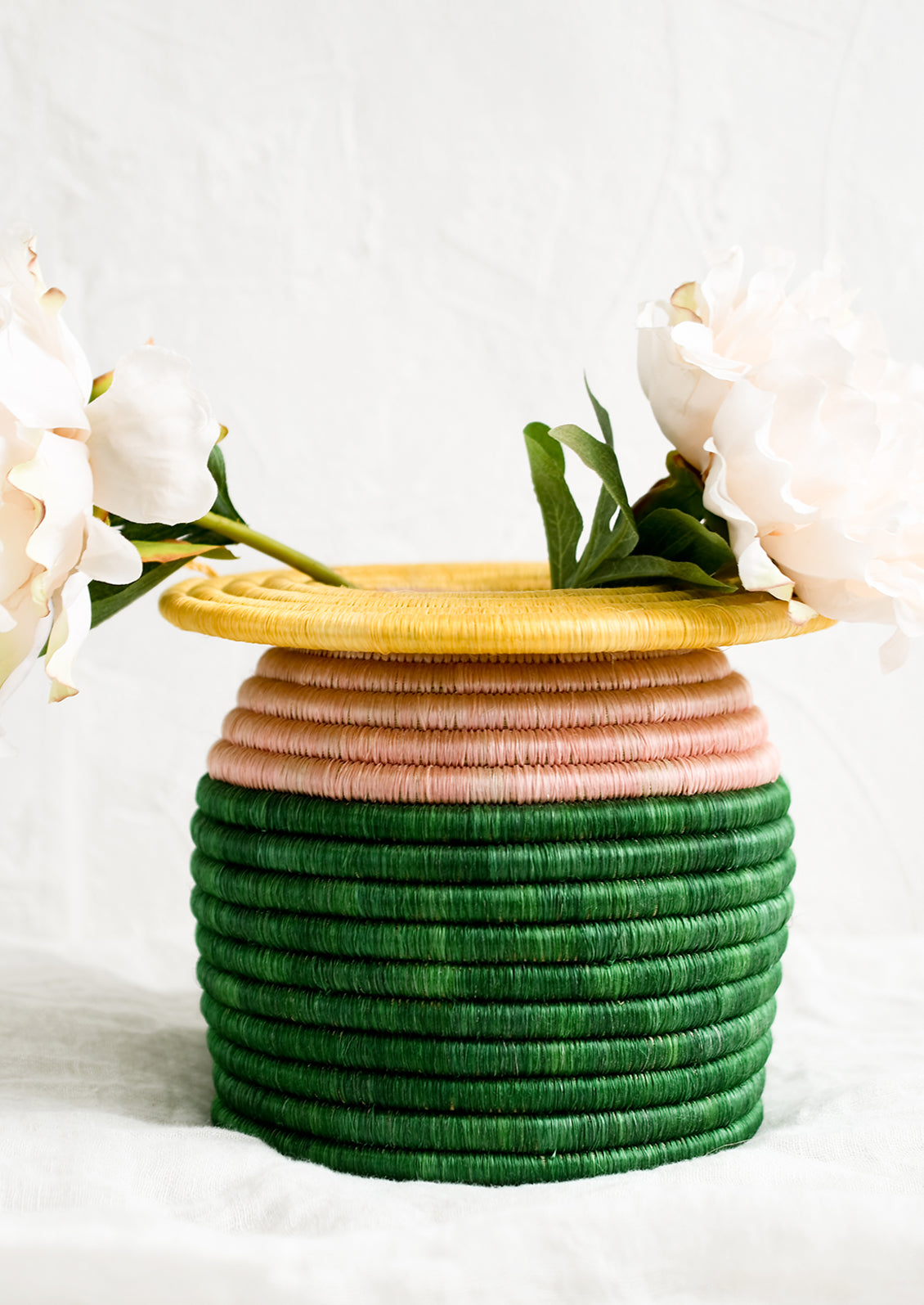 A color blocked, woven sweetgrass vase with peonies.