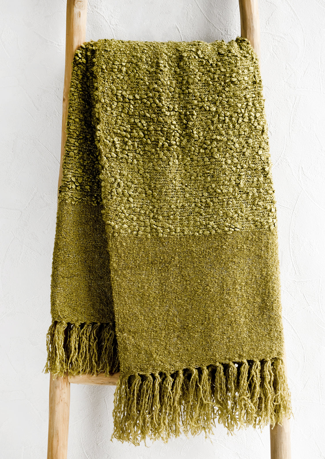 A moss green boucle throw with tassel trim.