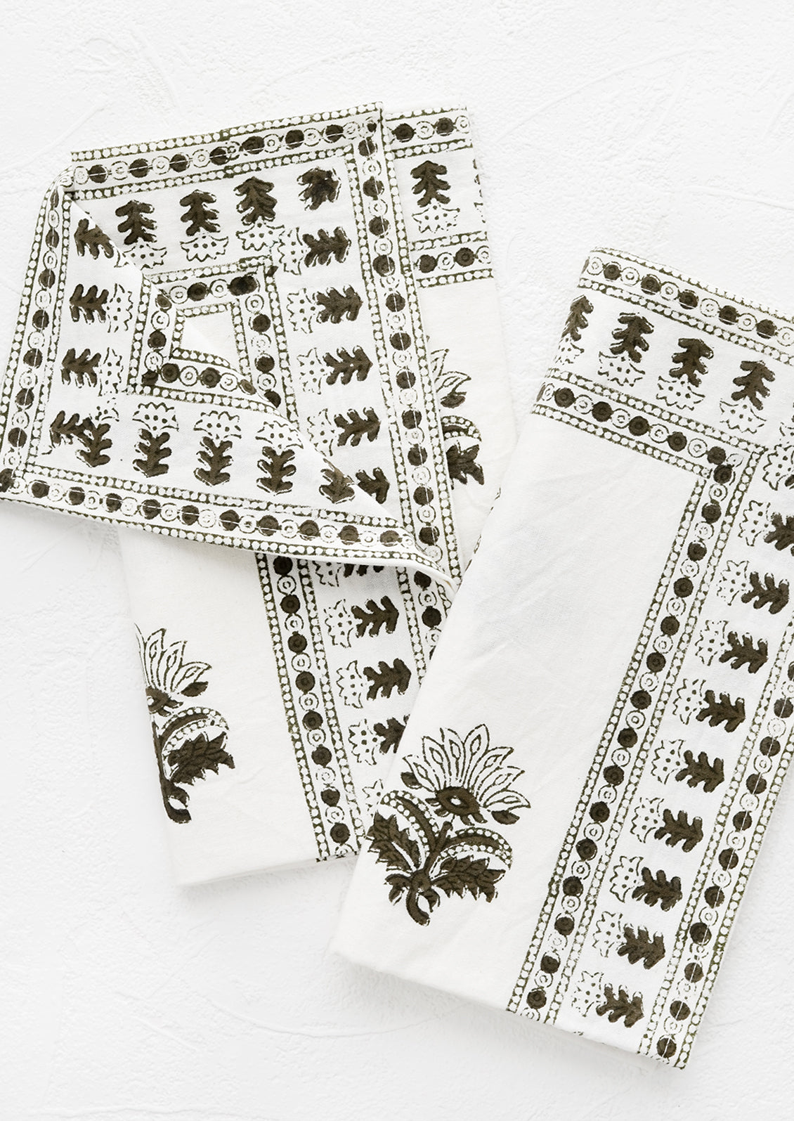 A pair of white napkins with block printed motif in moss green.