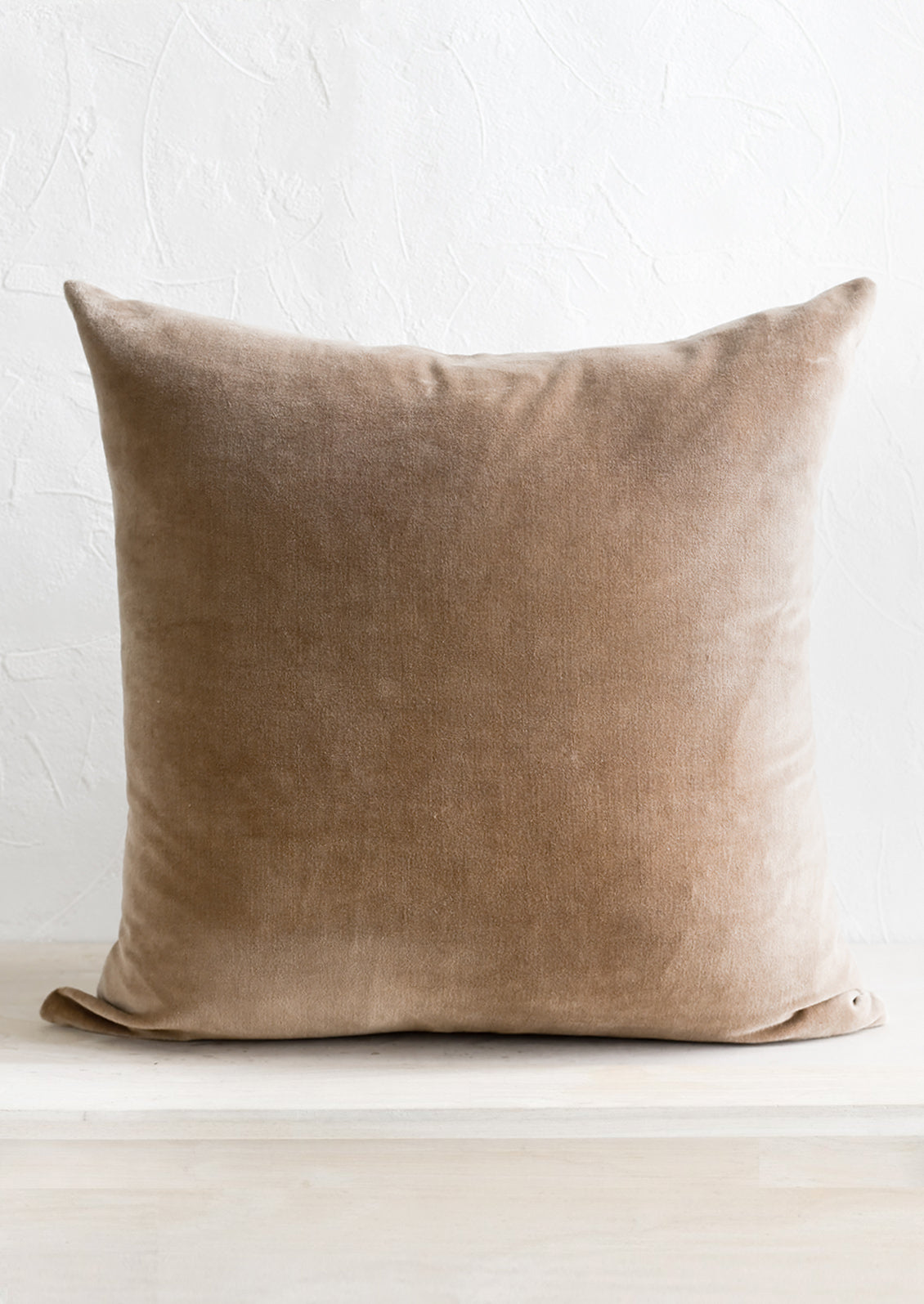 A square velvet throw pillow in taupe.
