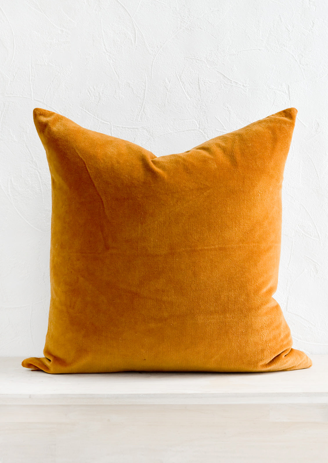 A square velvet throw pillow in warm amber color.