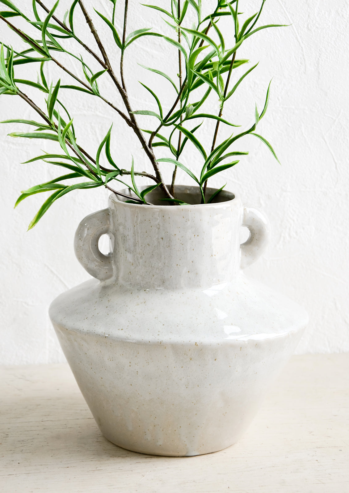 Grey ceramic vase in askew silhouette with green leaved branches.