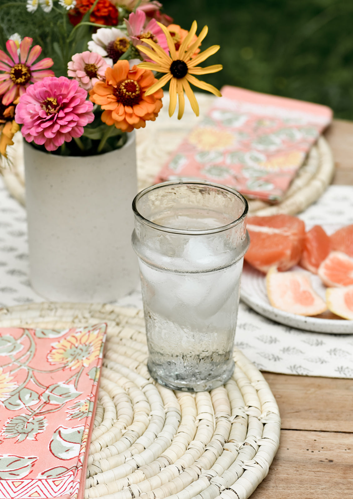 A table setting with round straw placemats and water glass.