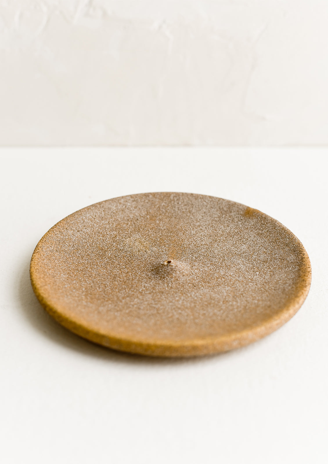 A round ceramic incense holder in matte sandy brown.